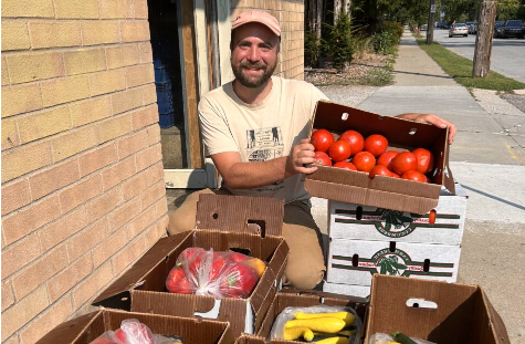  Will Moyer the Food Hub Man年龄r at 阿格斯农场站 stands behind several boxes of produce